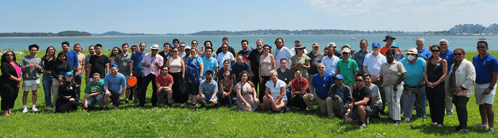 Group photo of IT Staff from the Barbecue event held in August of 2023 pictured on the lawn outside of the Campus Center with harbor in background.